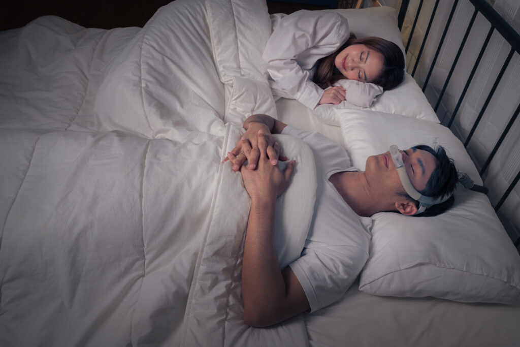 A couple sleeping in bed and a man wearing a CPAP machine in El Paso.